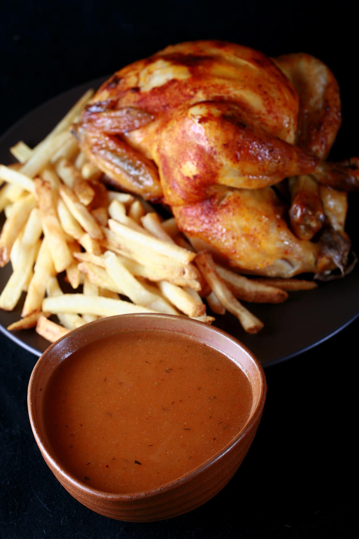 A large bowl of copycat Swiss Chalet Sauce next to a roasted chicken and fries.