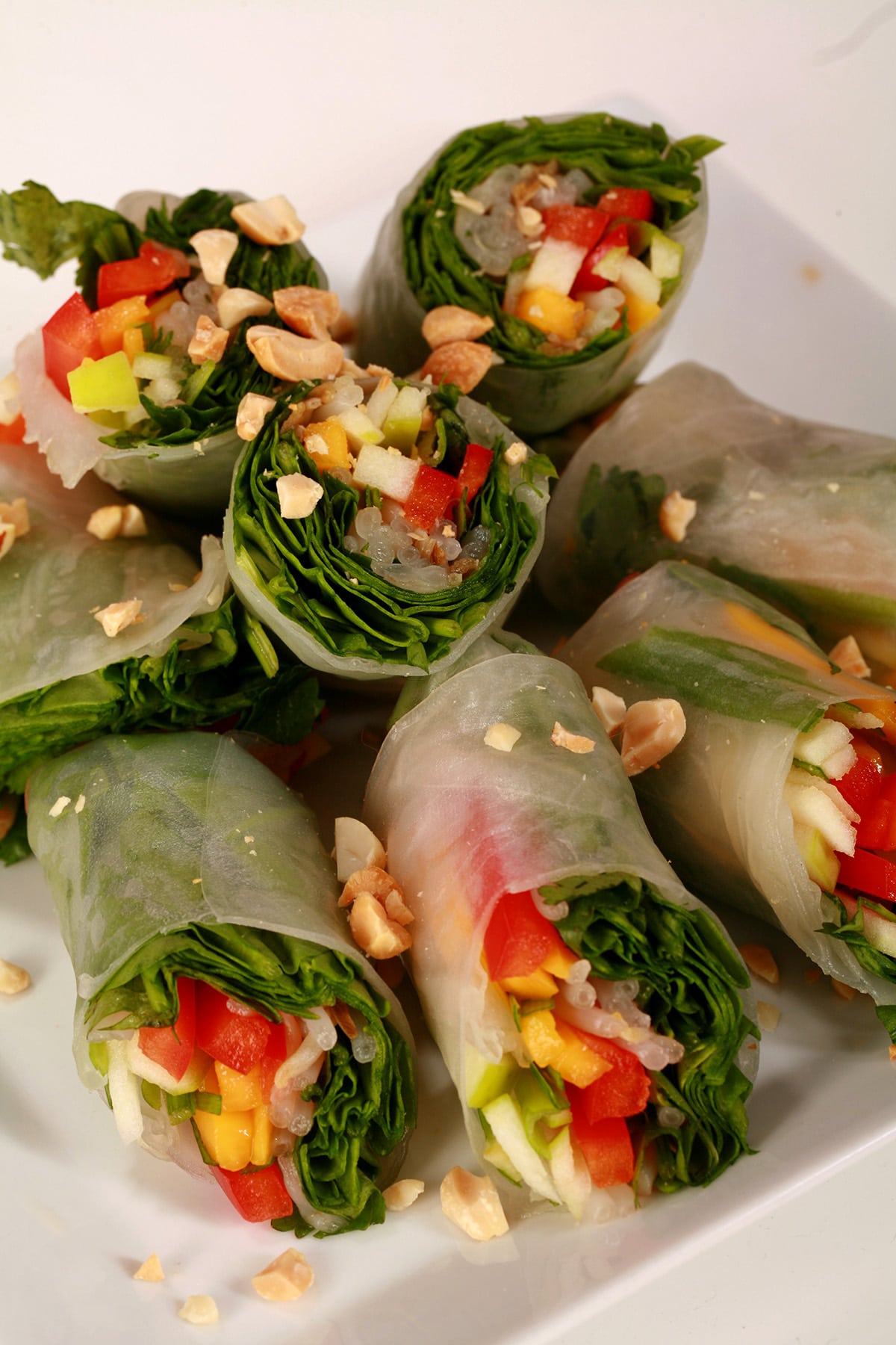 Several vegetarian salad rolls on a plate. They are filled with spinach, apples, mango, peppers, green onions, mint, and more.