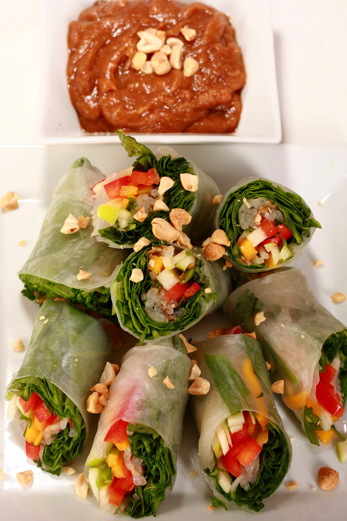 Several vegetarian salad rolls on a plate. They are filled with spinach, apples, mango, peppers, green onions, mint, and more.