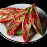 A plate with several pieces of green, red, and white marbled candy cane biscotti.