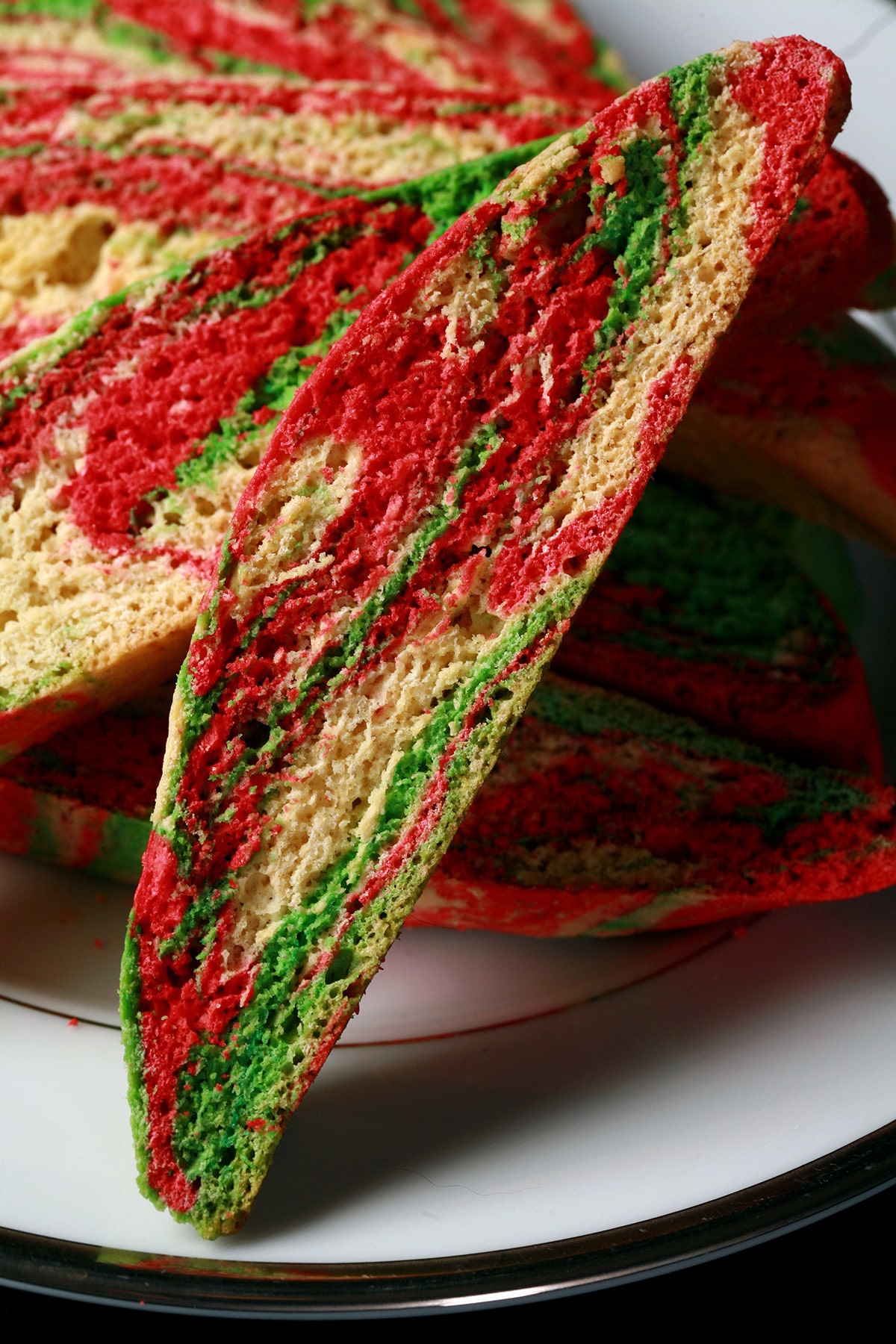 A plate with several pieces of green, red, and white marbled candy cane biscotti.