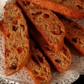 Several pieces of fruitcake biscotti, piled on a doily covered plate.