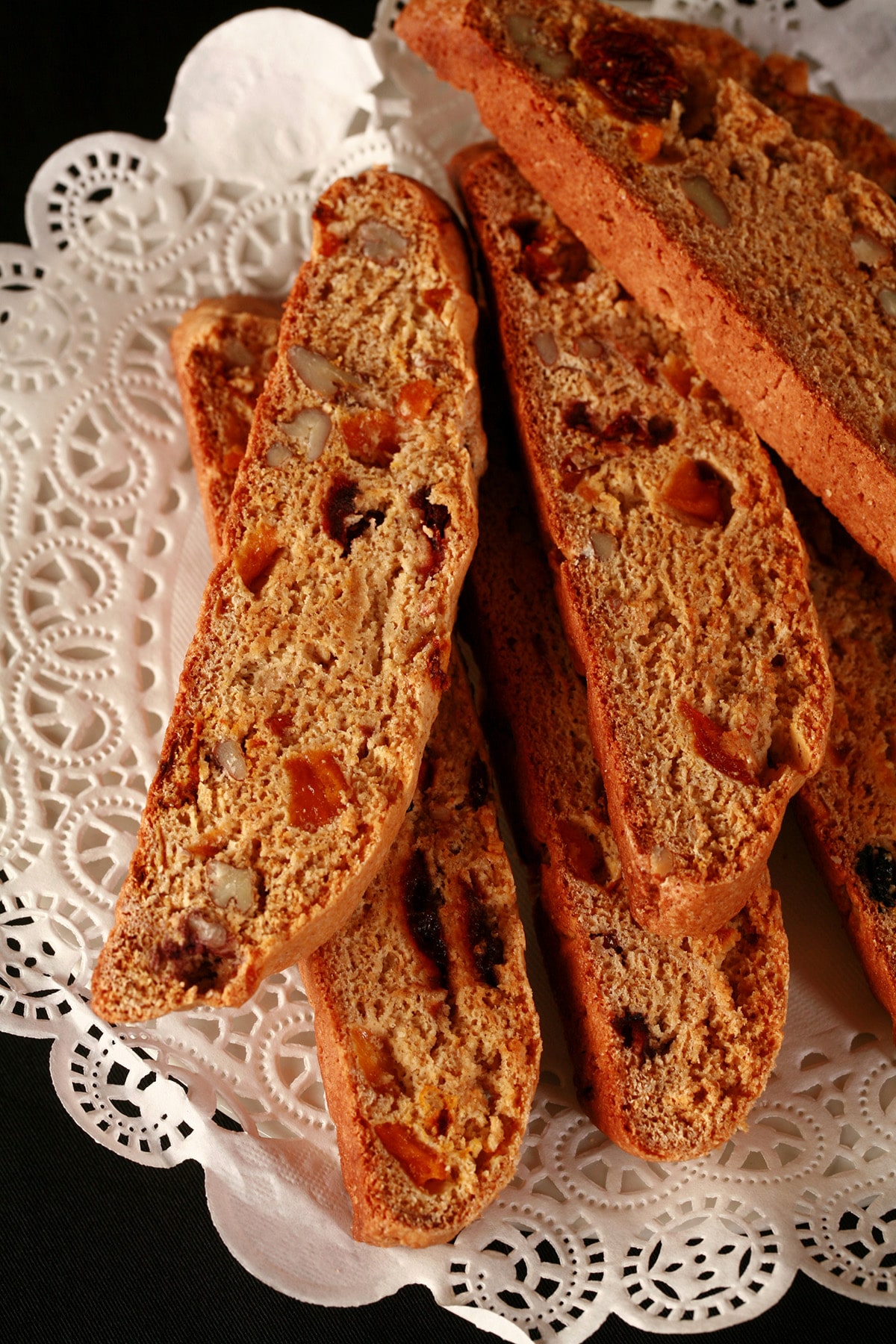 Several pieces of fruitcake biscotti, piled on a doily covered plate.