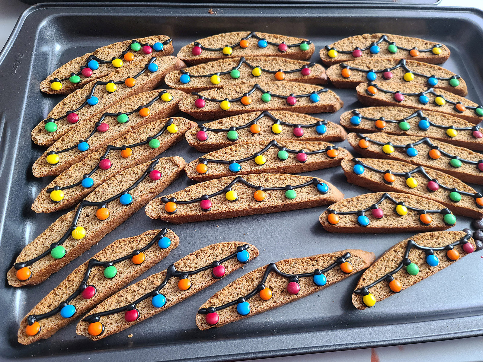 A pan of gingerbread biscotti decorated to look like it's strung with Christmas lights.