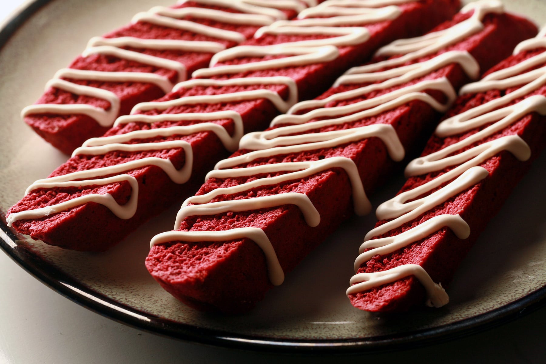 4 red velvet biscotti on a plate. They are each drizzled with a white glaze.