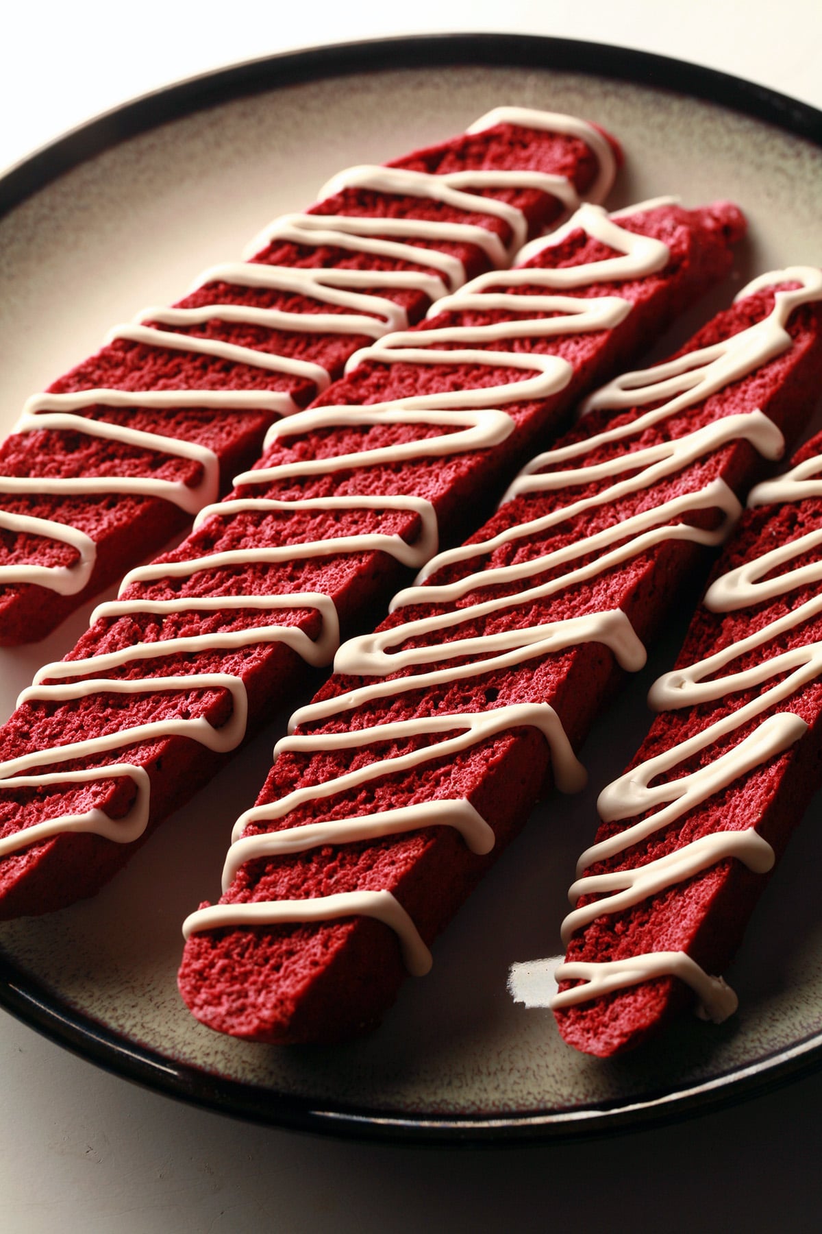 4 red velvet biscotti on a plate. They are each drizzled with a white glaze.