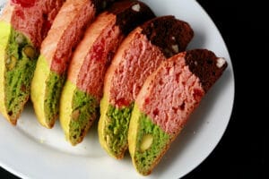 A white plate with several pieces of spumoni biscotti - strips of green, pink, and chocolate.
