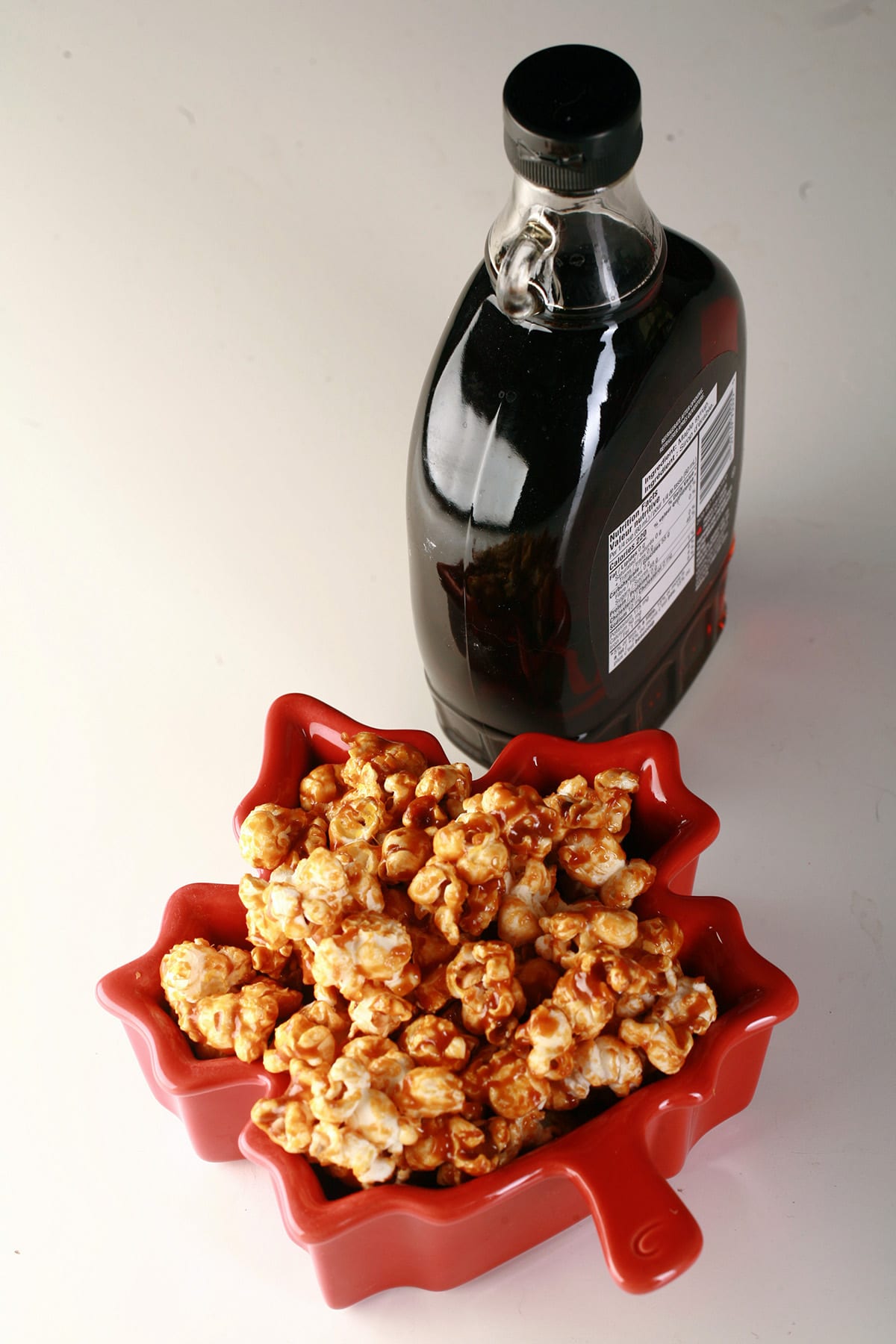 A bowl of maple syrup caramel poporn in front of a bottle of maple syrup.