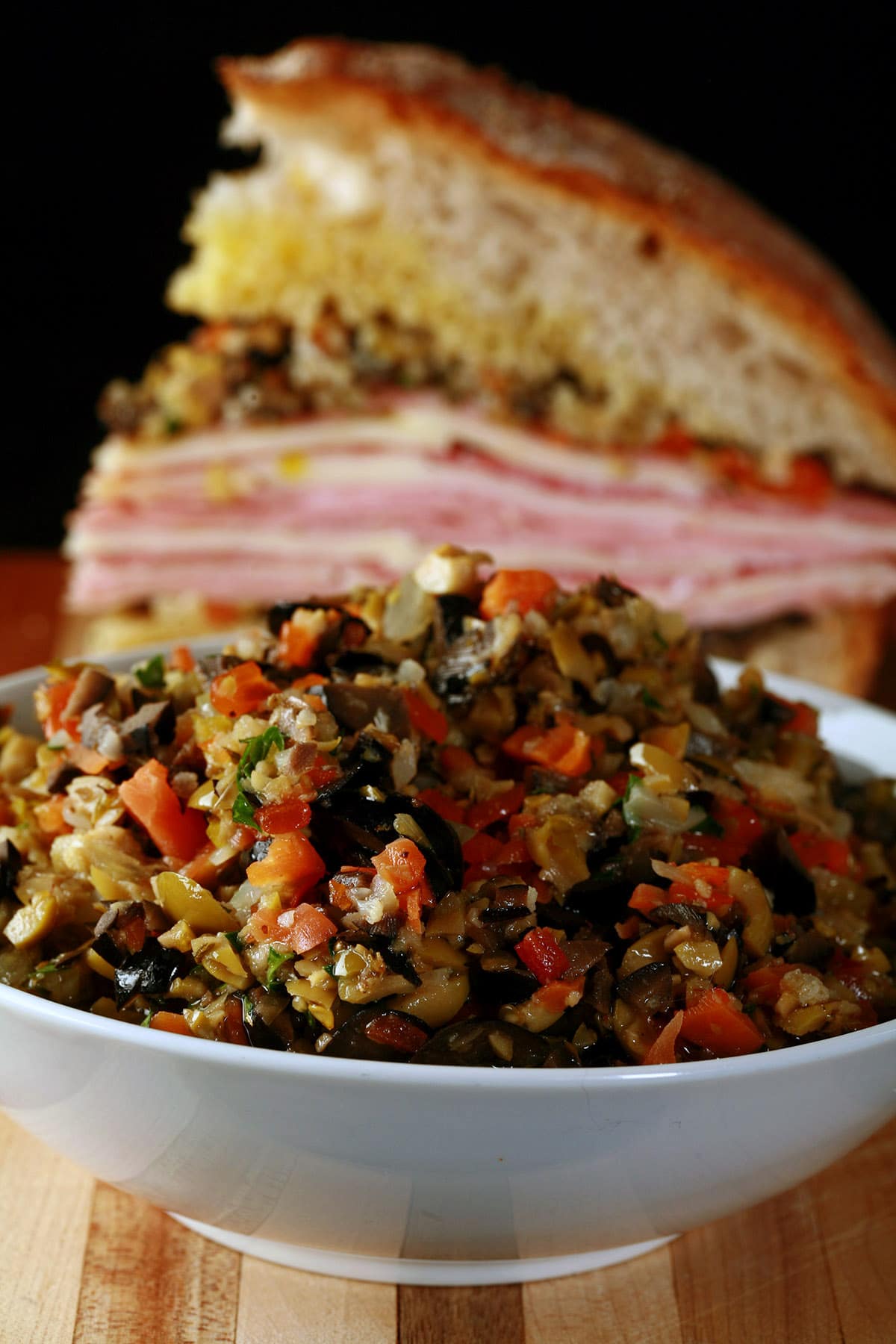 A bowl of olive salad in front of a wedge of muffaletta.