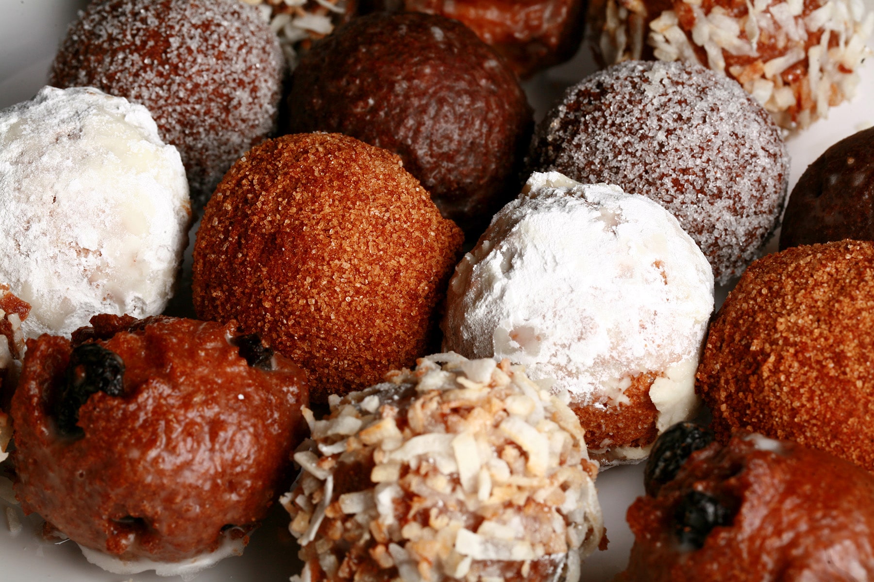 A close up view of an assortment of homemade donut holes: Toasted coconut, chocolate glazed, cinnamon sugar, powdered sugar, and dutchie versions are all visible.