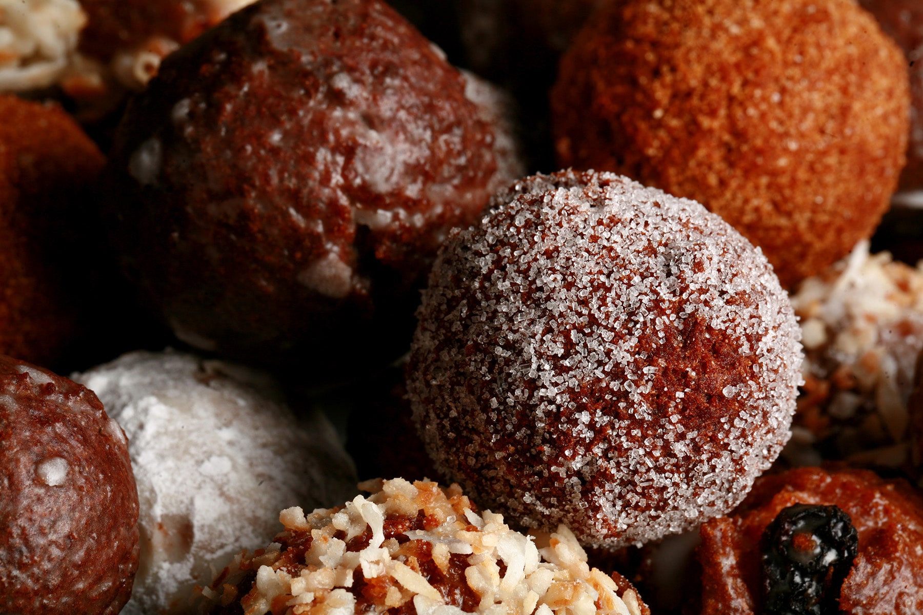 A close up view of an assortment of homemade doughnut holes: Toasted coconut, chocolate glazed, cinnamon sugar, powdered sugar, and dutchie versions are all visible.