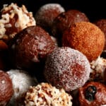 A close up view of an assortment of homemade donut holes: Toasted coconut, chocolate glazed, cinnamon sugar, powdered sugar, and dutchie versions are all visible.