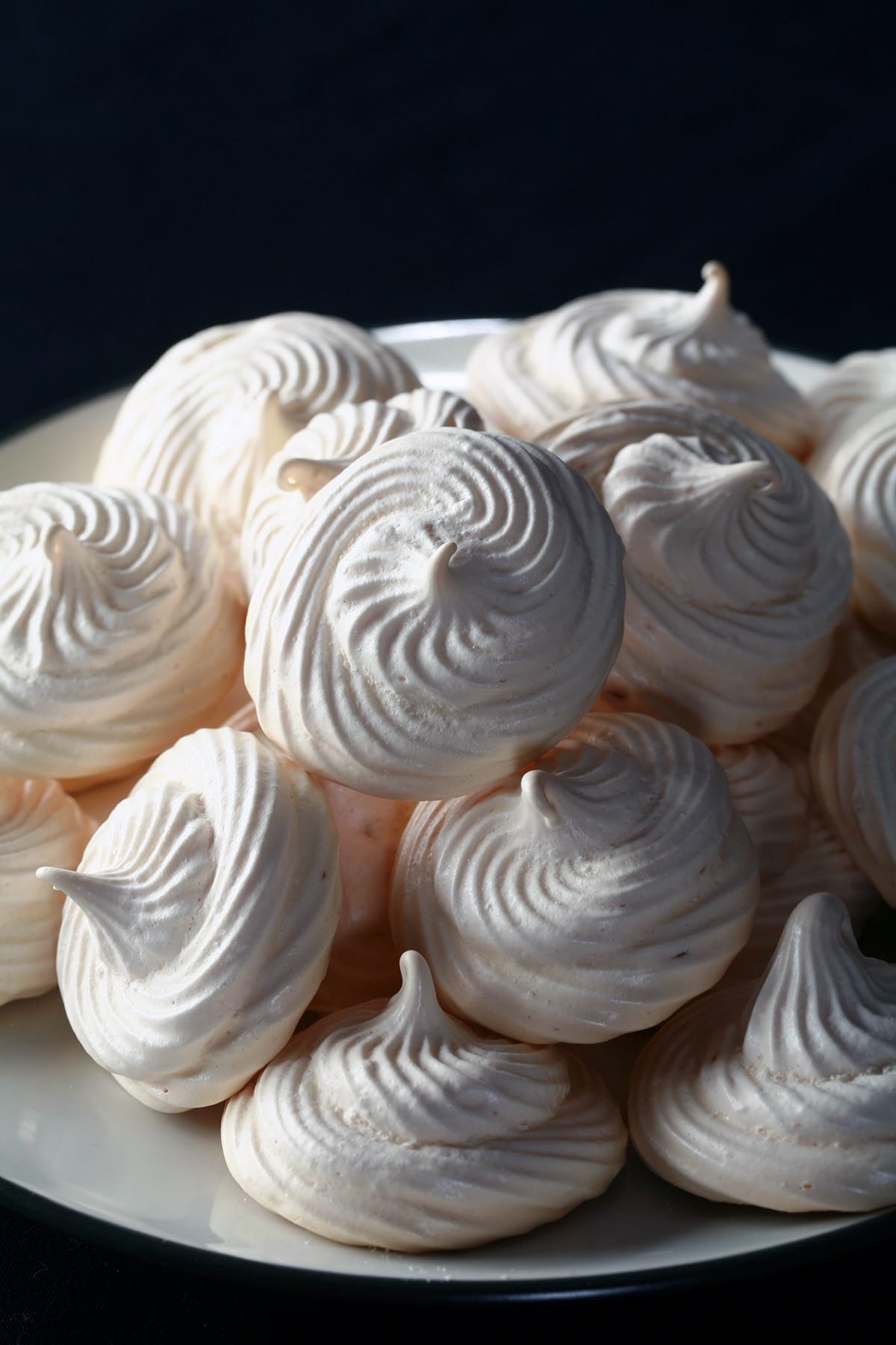 A plate piled high with swirl shaped malted milk meringue cookies.