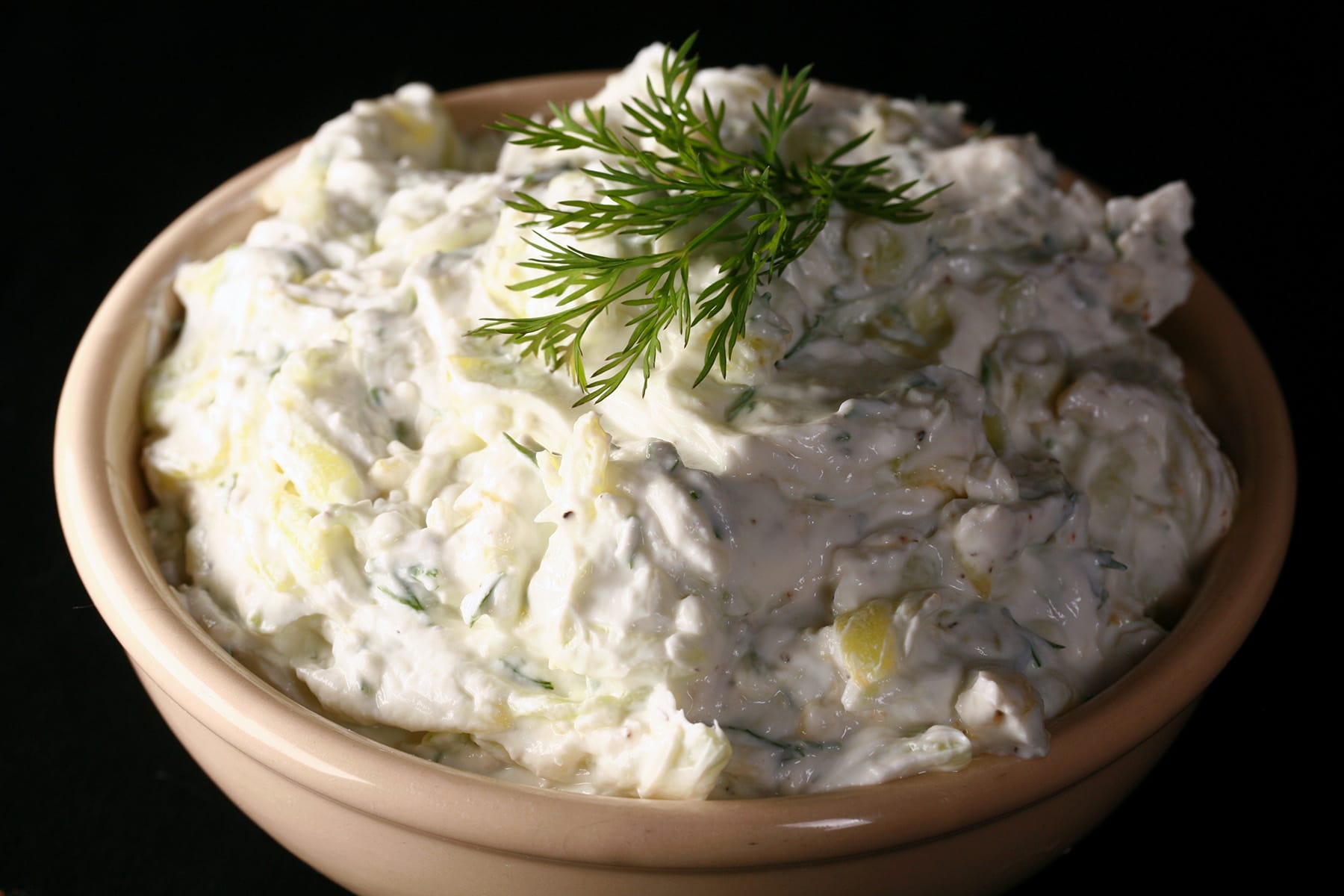 A bowl of thick tzatziki dip, garnished with fresh dill.