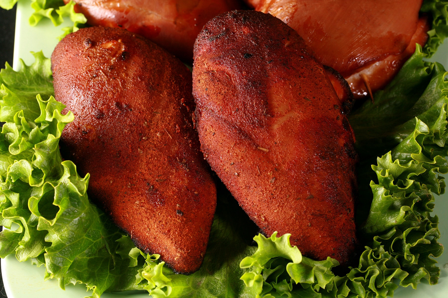 Several smoked chicken breasts on a platter of lettuce.