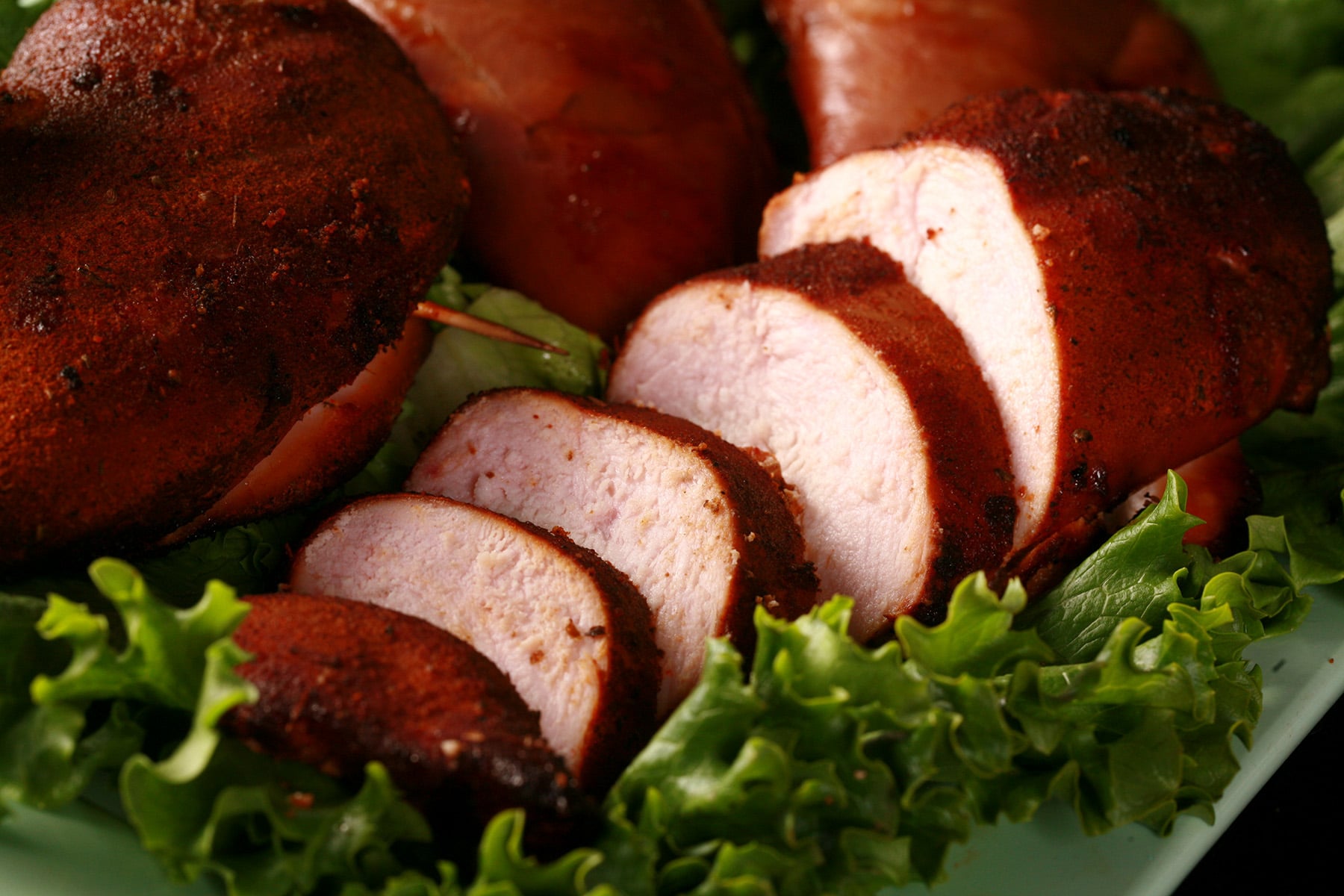 Several pieces of smoked chicken breast on a bed of lettuce.