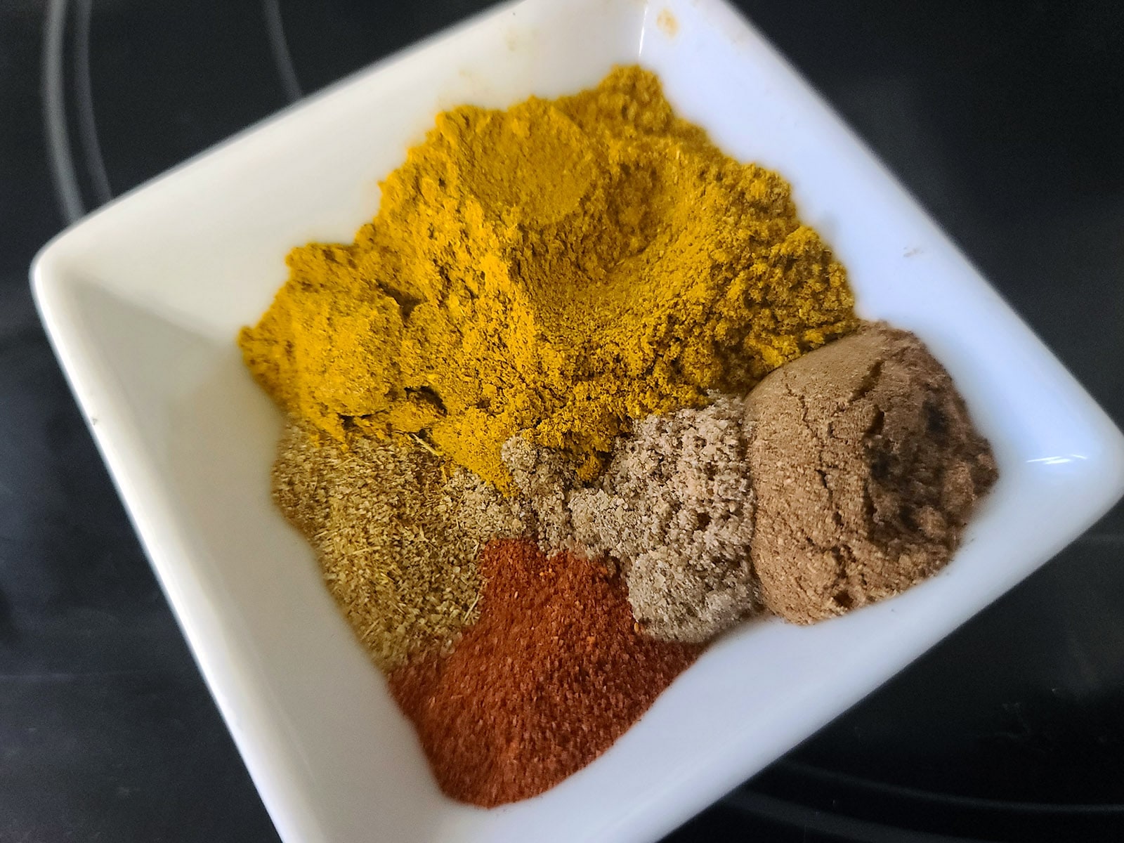 A bowrl of brightly coloured Indian spices.