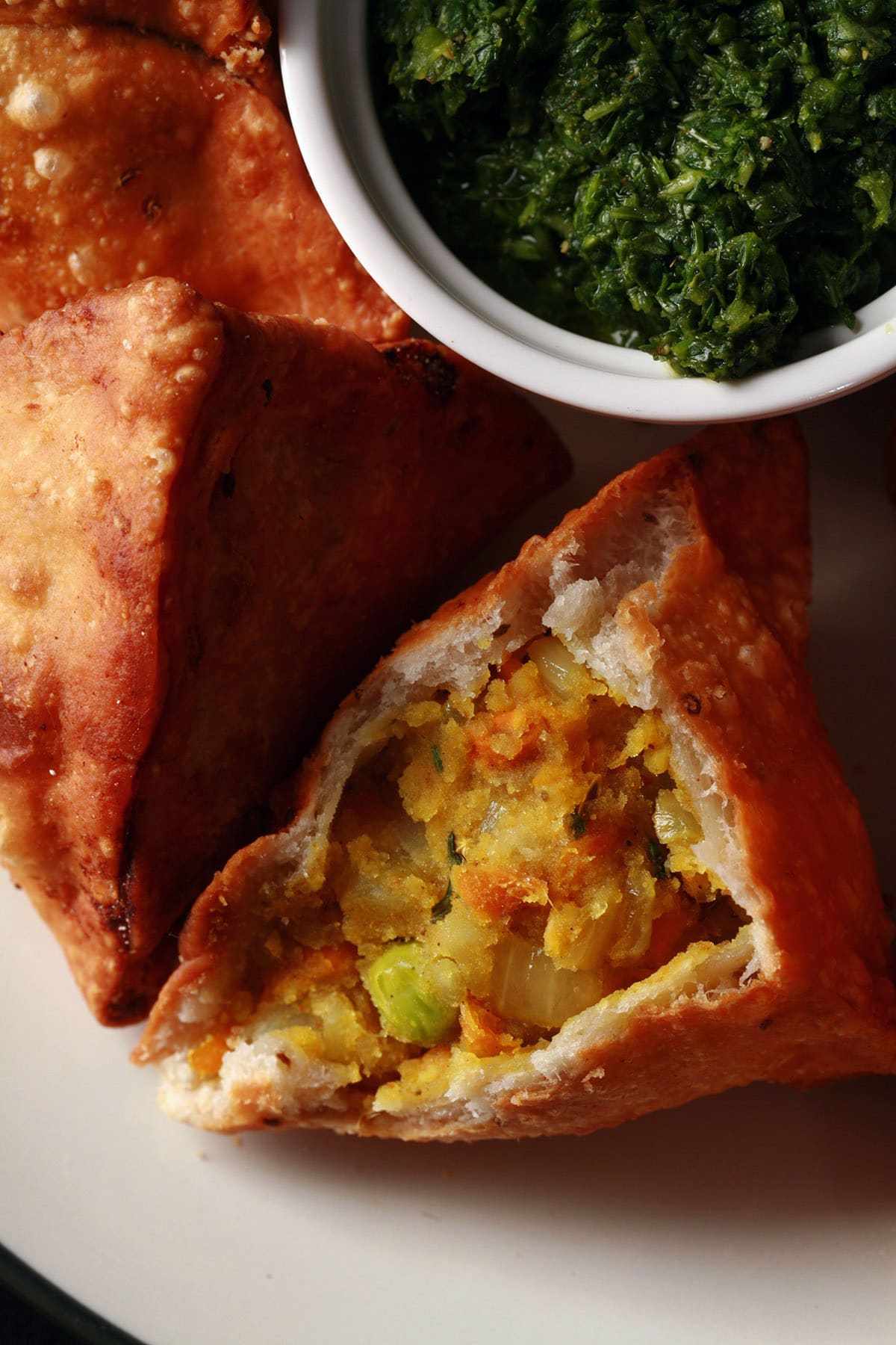 A plate of homemade vegetarian samosas, with a small bowl of cilantro mint chutney.