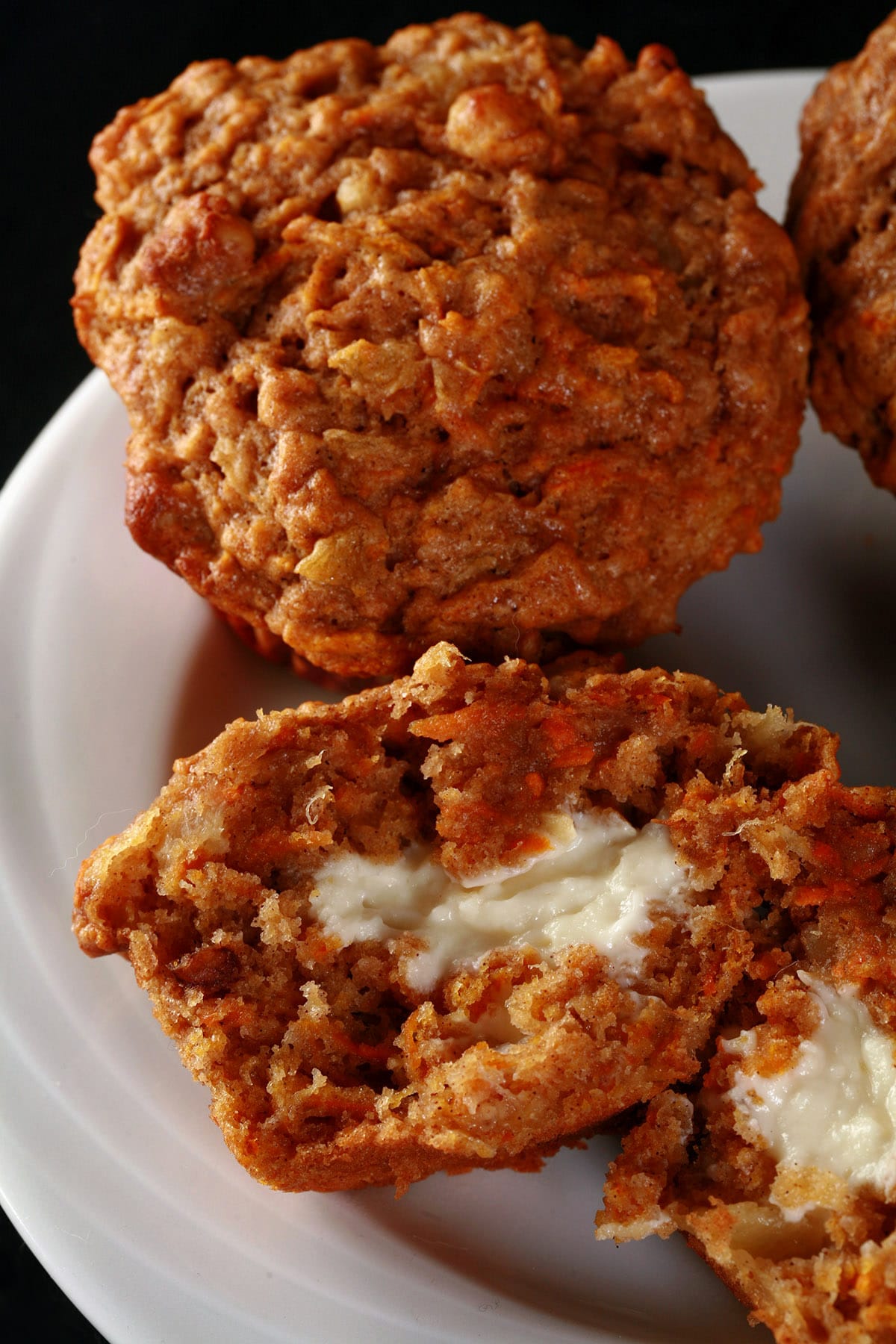 1 whole carrot cake muffin on a plate, plus another split in half to show the cream cheese filling.