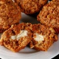 3 whole carrot cake muffins on a plate, plus another split in half to show the cream cheese filling.