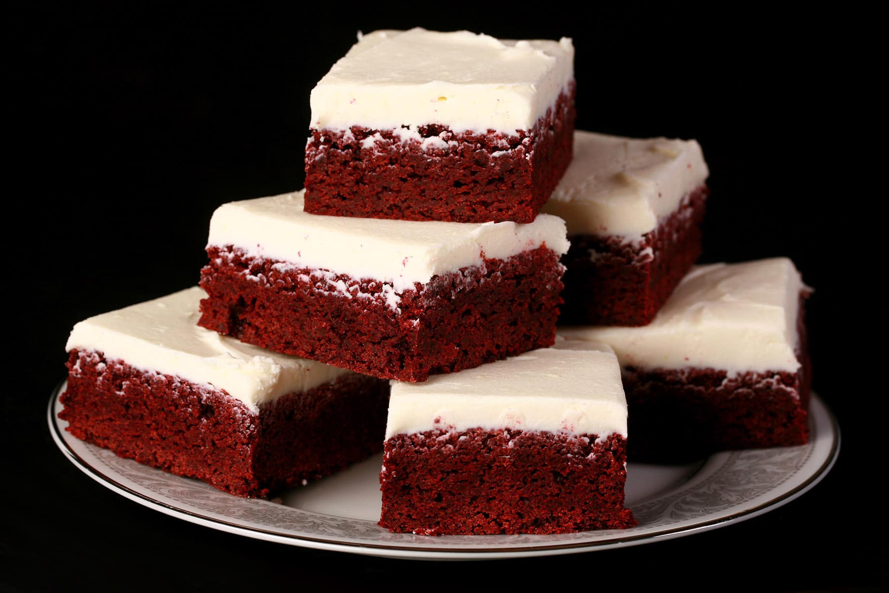 A plate stacked with red relvet brownies, each frosted with cream cheese icing.