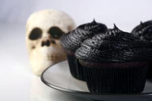 2 black velvet cupcakes on a white plate, with a skull in the background.