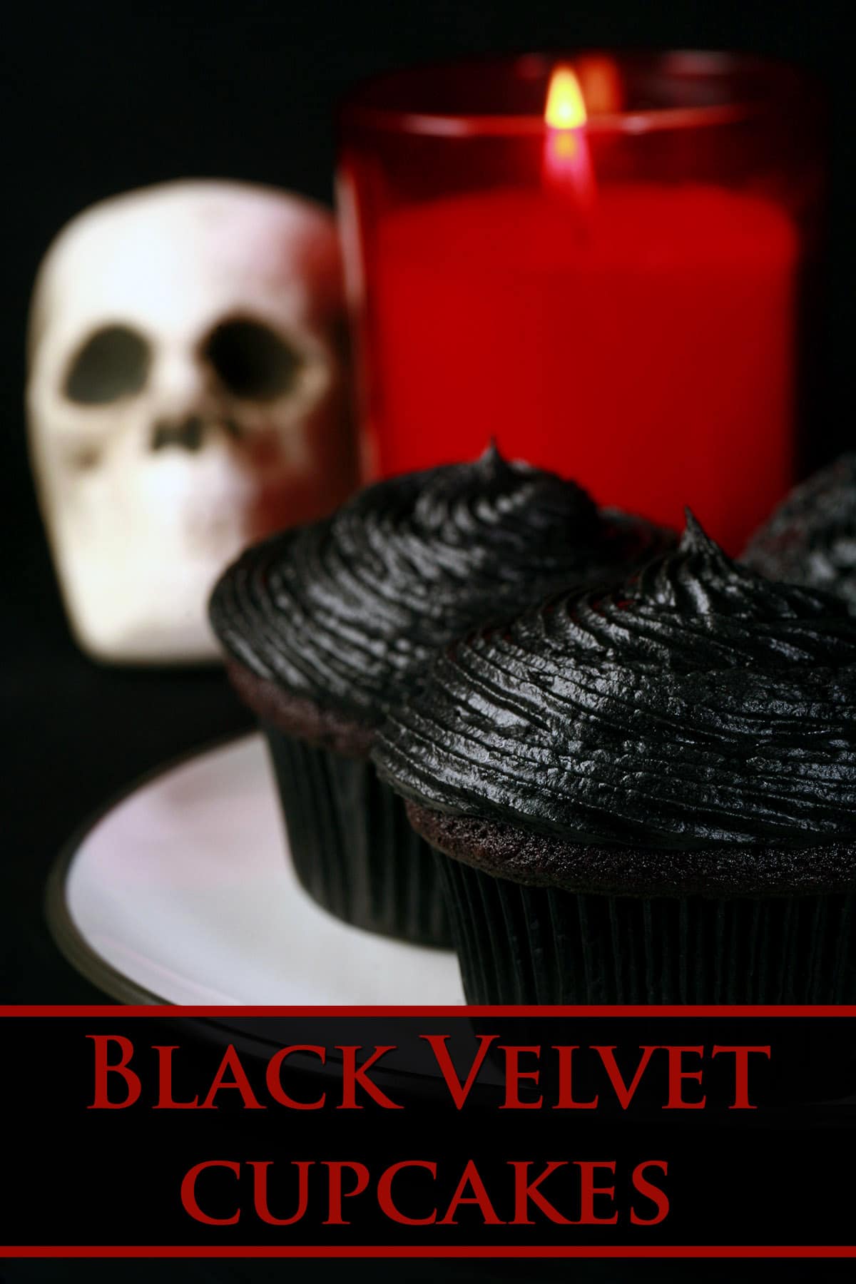 2 black velvet cupcakes on a white plate, with a skull and red candle in the background.