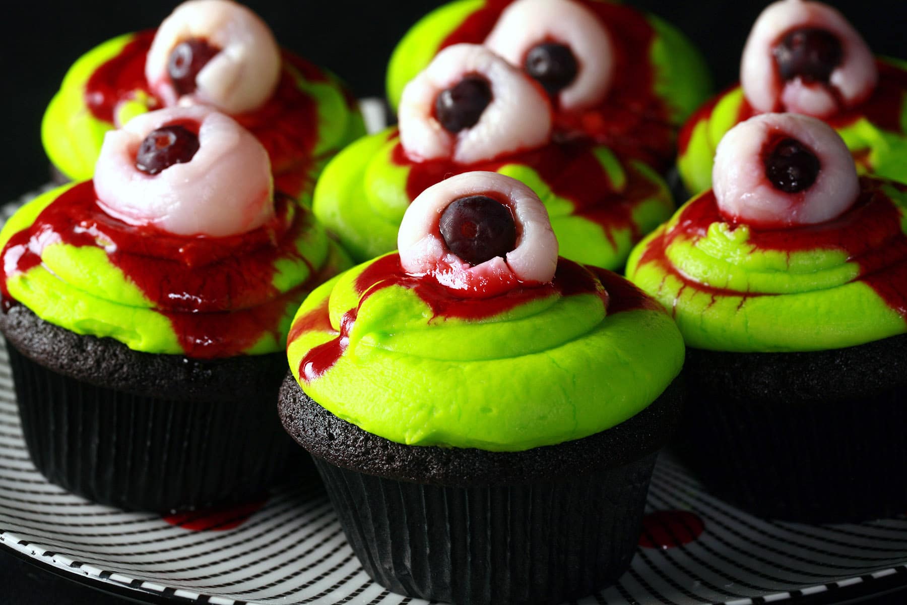 Several Halloween cupcakes on a plate. They have neon green frosting and a lychee eyeball on top.