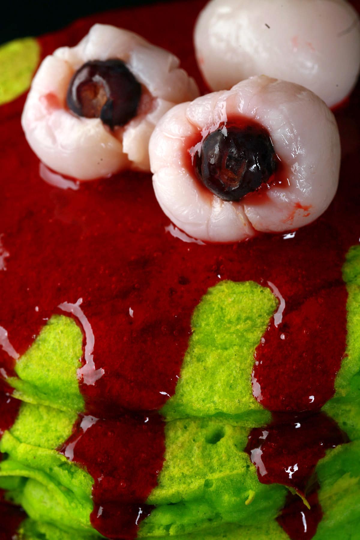 A stack of neon green bloody eyeball pancakes, with red syrup.
