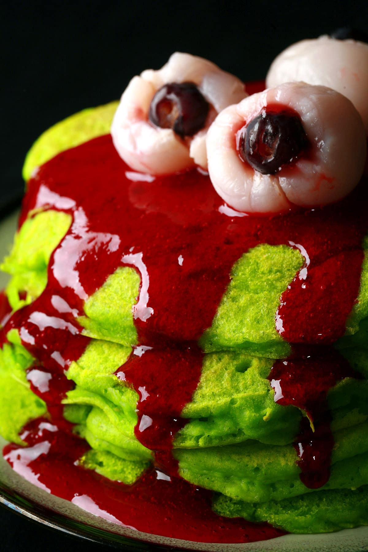 A stack of neon green Halloween pancakes with red sauce and lychee eyeballs on top.