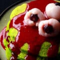 A stack of neon green Halloween pancakes with red sauce and lychee eyeballs on top.