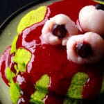 A stack of neon green Halloween pancakes with red sauce and lychee eyeballs on top.