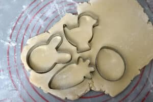 Sugar cookie dough rolled out and being cut into shapes with Easter cookie cutters.