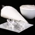 Traditional egg white royal icing in a bowl and a pastry bag, with 2 mixers on a plate.