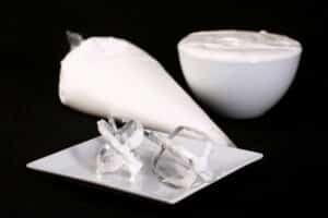Traditional egg white royal icing in a bowl and a pastry bag, with 2 mixers on a plate.