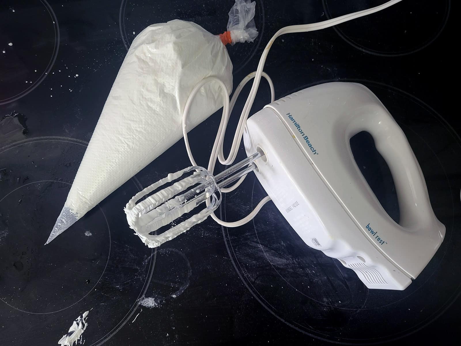 An electric hand mixer next to a pastry bag filled with royal icing.