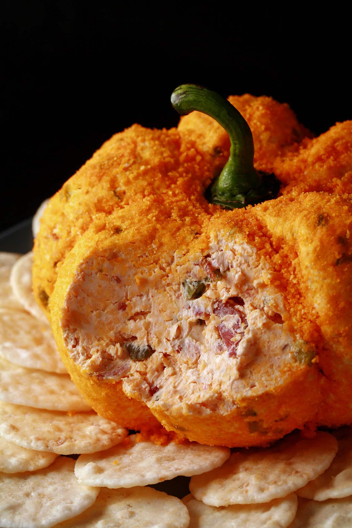 A pumpkin shaped cheese ball with bacon and jalapenos visible inside.