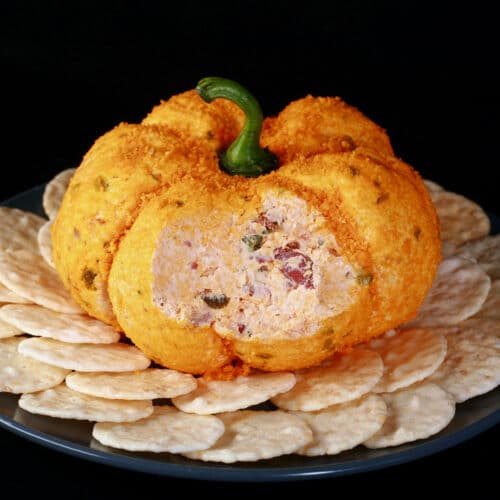 A pumpkin shaped cheese ball with bacon and jalapenos visible inside.