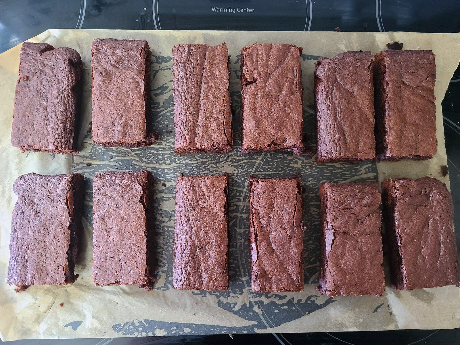 12 rectangular brownie bars lined up on a piece of parchment paper.