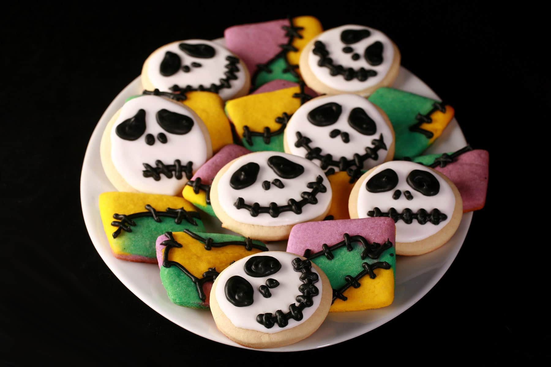 A mixed platter of Nightmare Before Christmas cookies: Jack Skellington face cookies & squares of Sally cookies that look like patchwork.