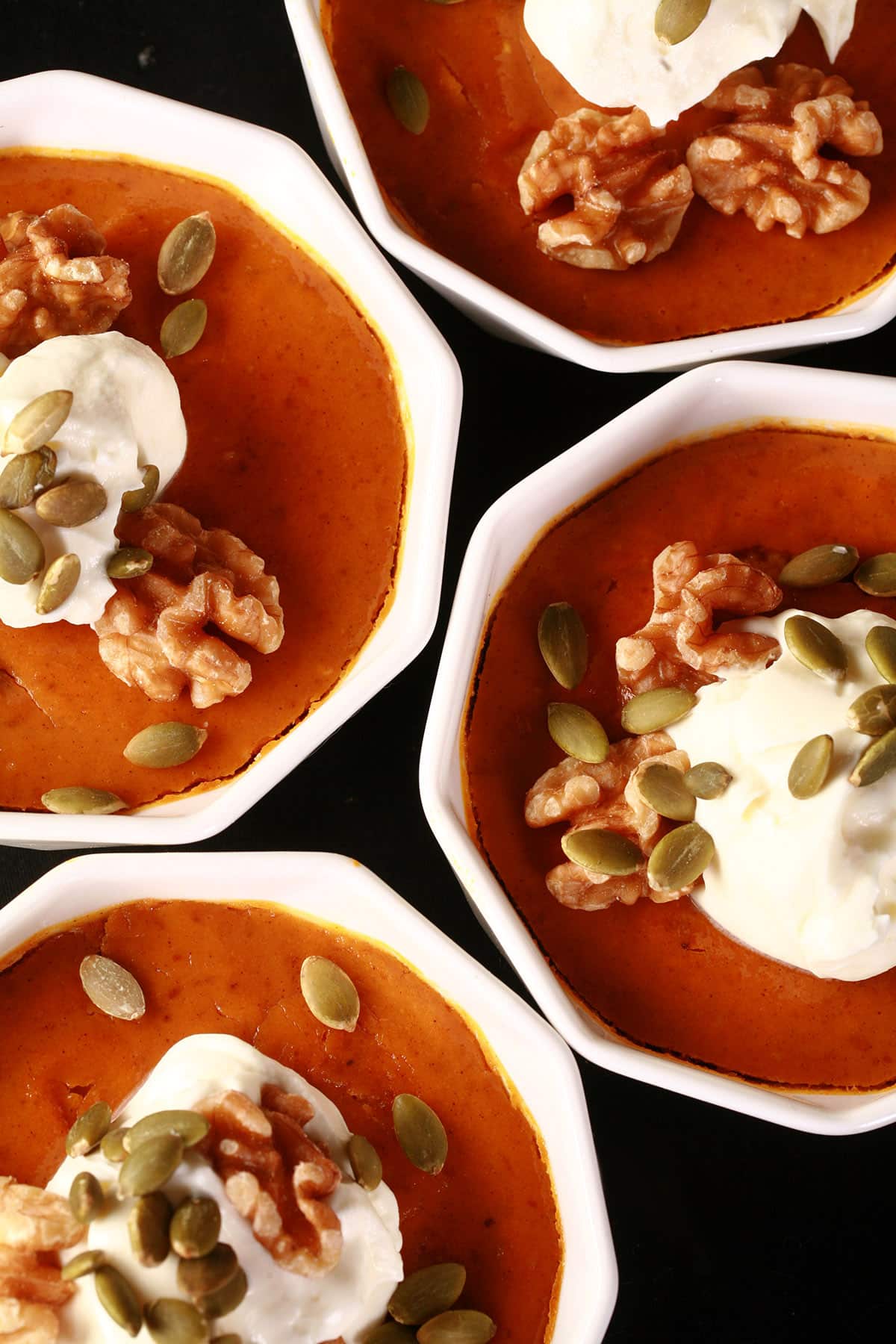 4 individual pumpkin custards topped with whipped cream, walnuts, and pumpkin seeds,