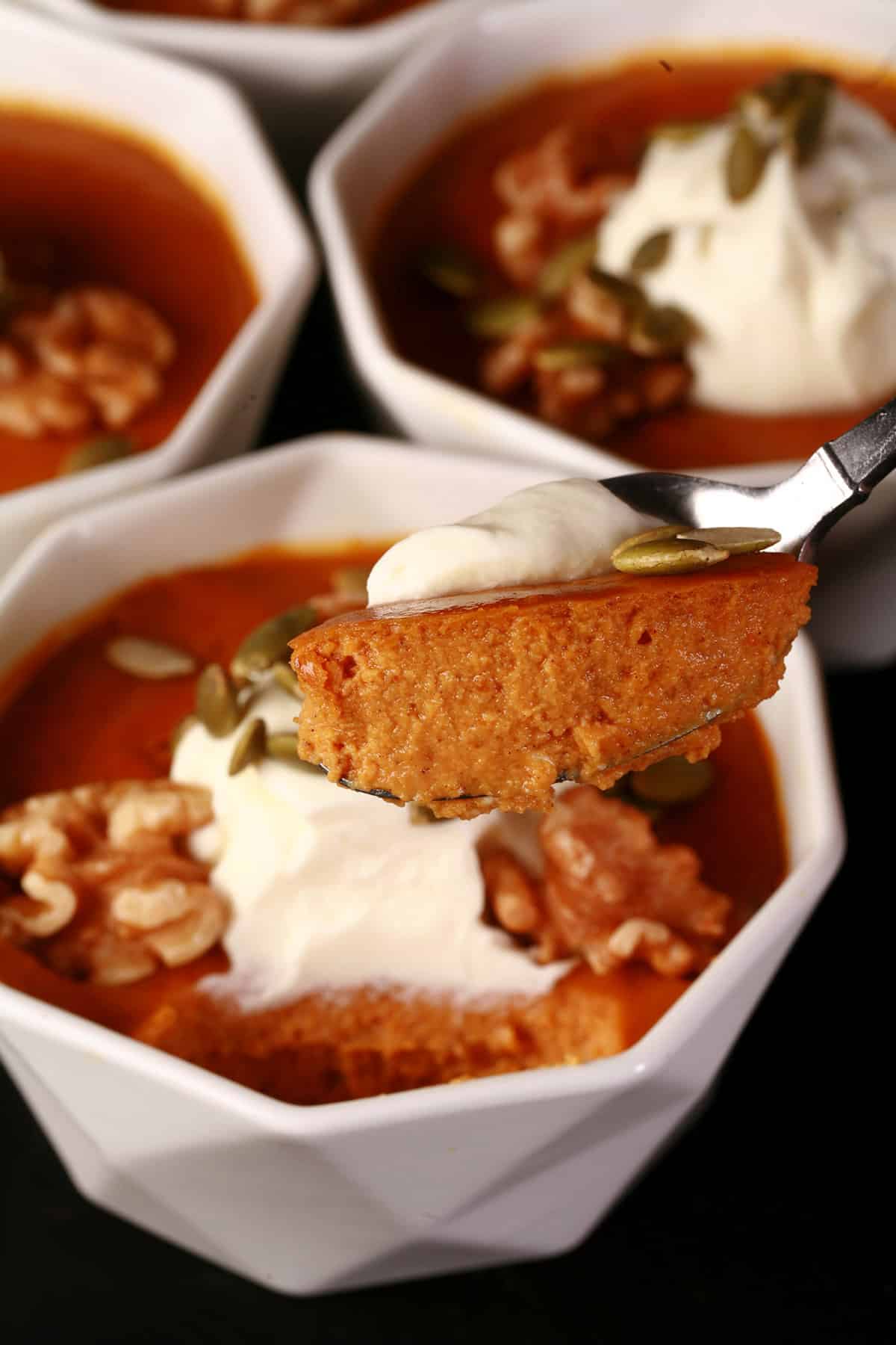 A ramekin of pumpkin pie custard with whipped cream and walnuts. A spoonful of custard is in the foreground.