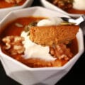 A ramekin of pumpkin pie custard with whipped cream and walnuts. A spoonful of custard is in the foreground.