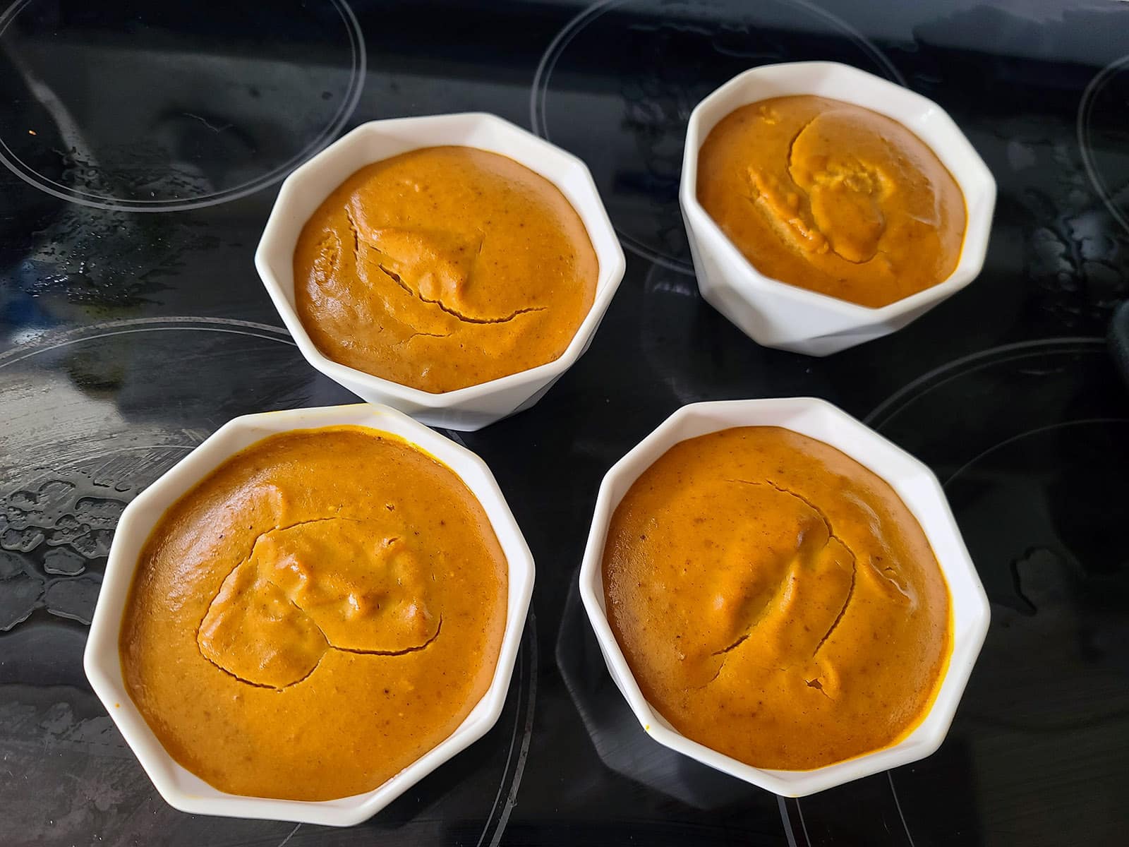 4 cooked pumpkin custards in ramekins on a stove top.