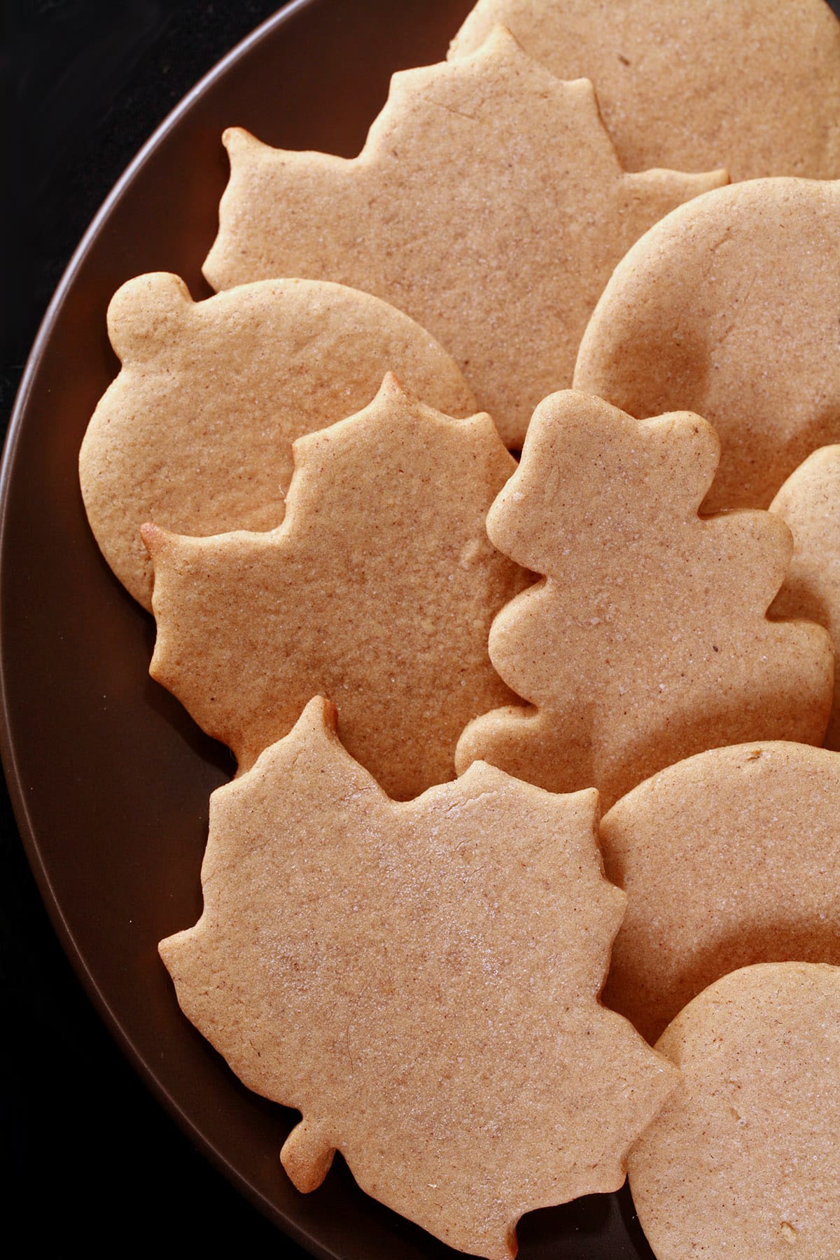 A plate of rolled cut-out pumpkin spice cookies in apple, pumpkin, and leaf shapes.