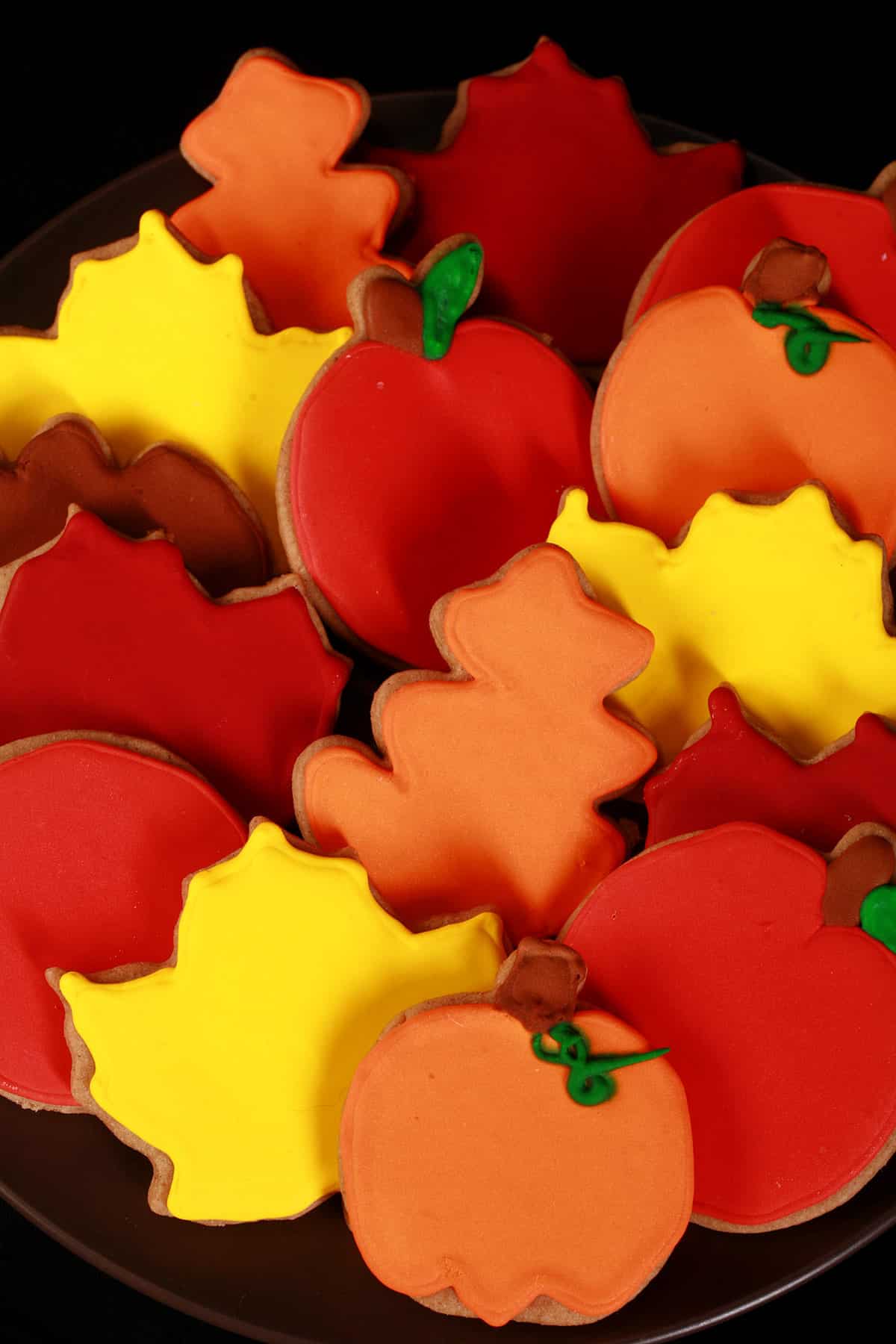 A plate of pumpkin spice sugar cookies decorated in brightly colored royal icing to look like apples, pumpkins, and fall leaves.