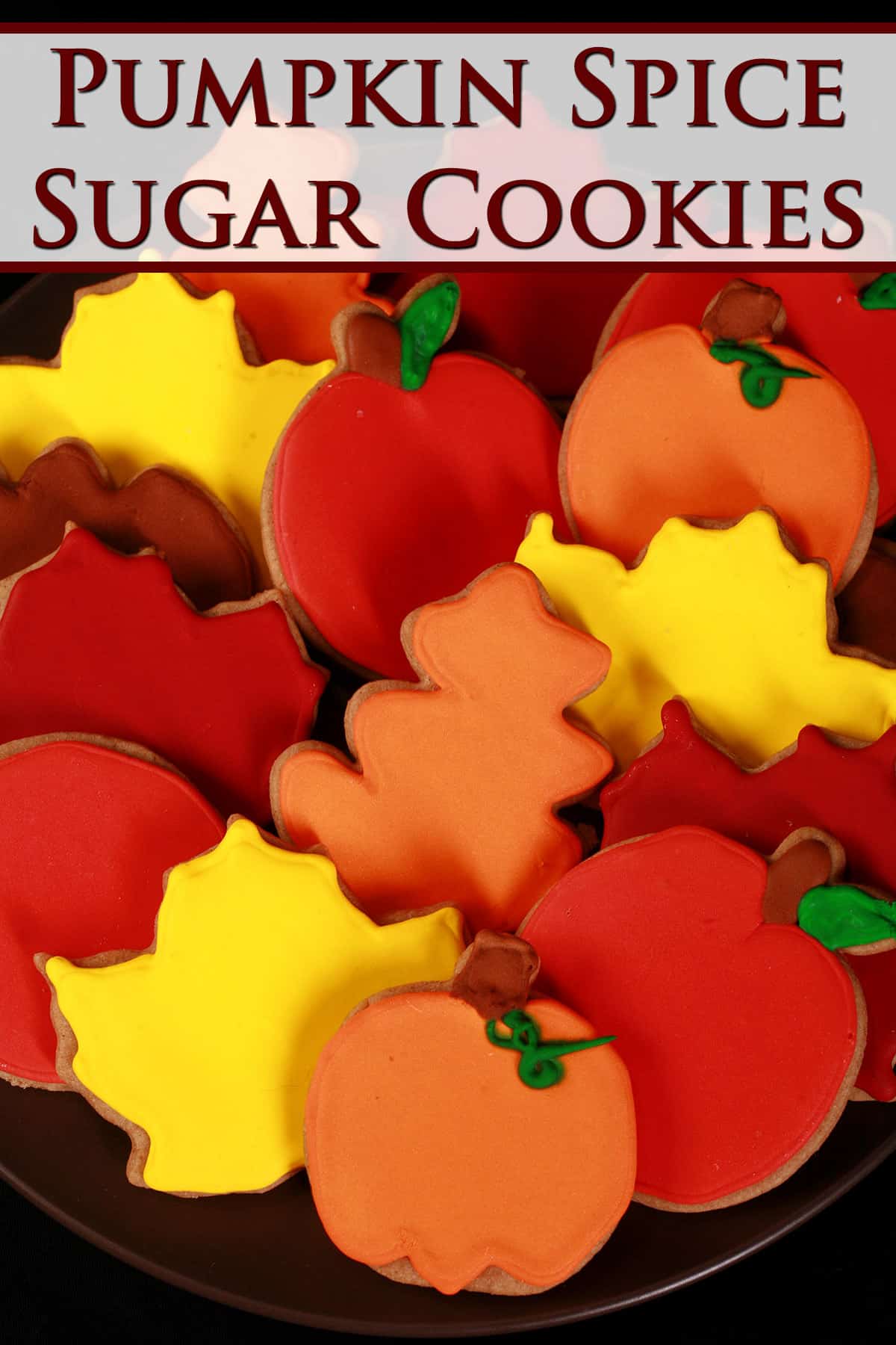A plate of pumpkin spice sugar cookies decorated in brightly colored royal icing to look like apples, pumpkins, and fall leaves.
