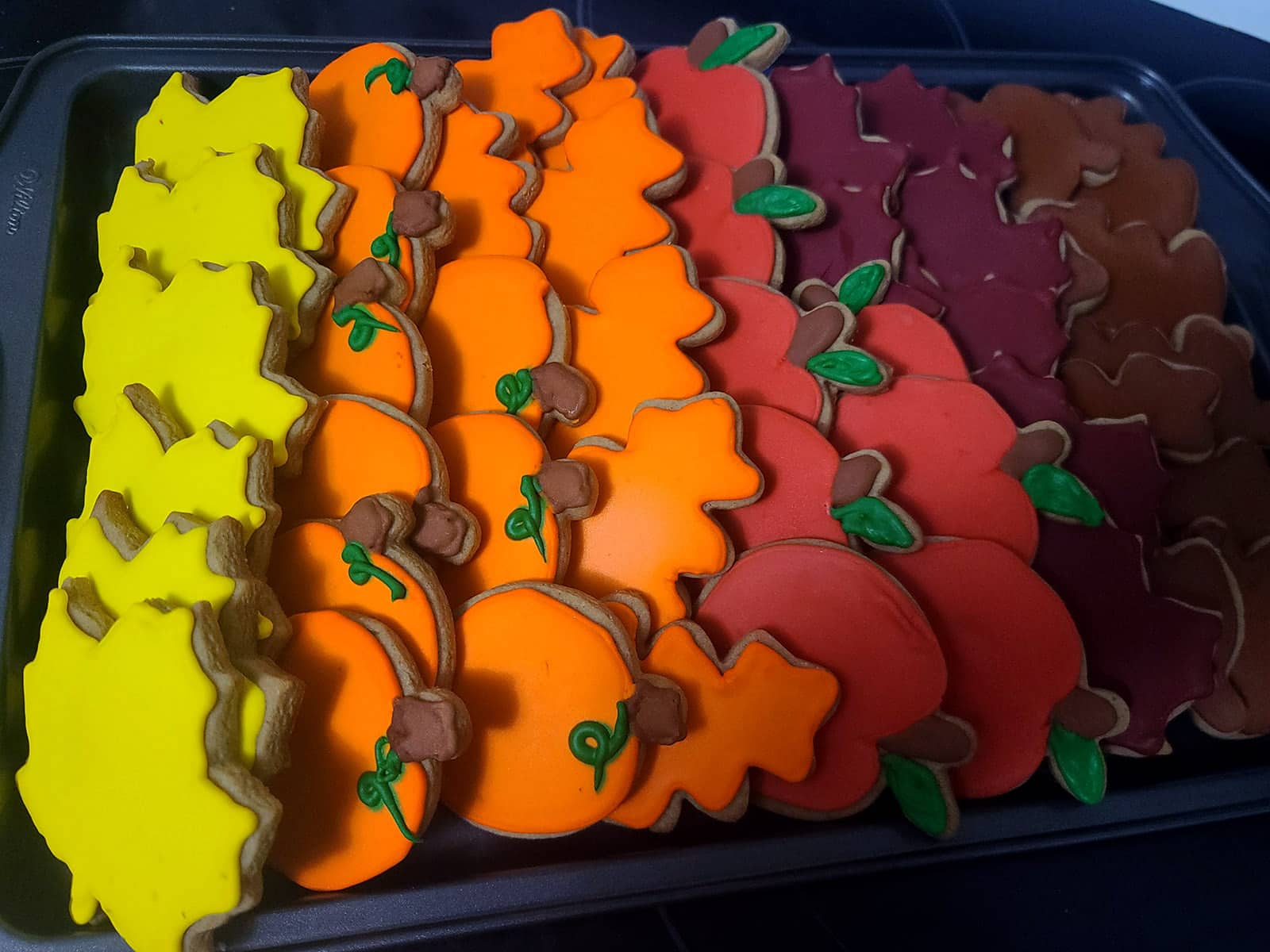 A tray of pumpkin spice sugar cookies decorated in brightly colored royal icing to look like apples, pumpkins, and fall leaves.