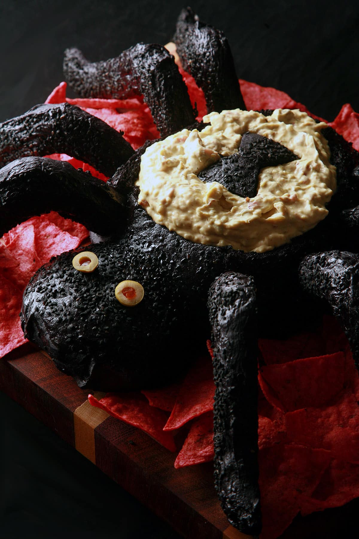 A black spider bread bowl, filled with dip and surrounded by red tortilla chips.