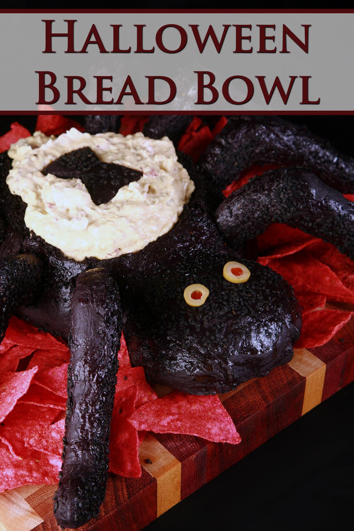 A black spider bread bowl, filled with dip and surrounded by red tortilla chips.